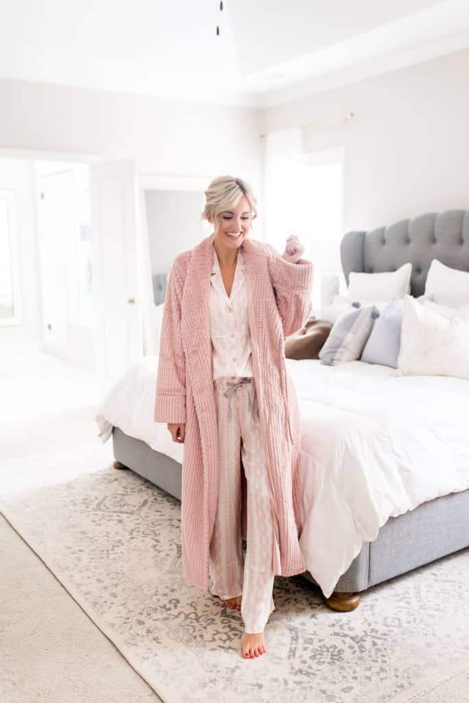 woman standing in bedroom wearing woman in bedroom wearing cozy pink soma intimates long sleeve top and pants matching pajama set with pink bath robe