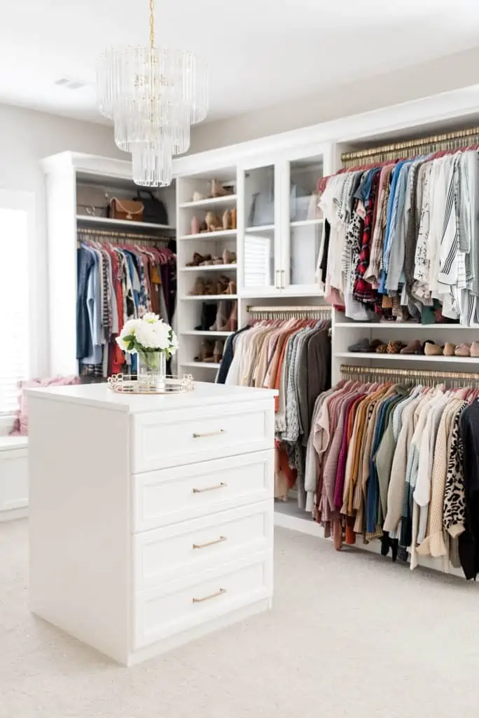 custom walk in closet with white center console of drawers and chandelier